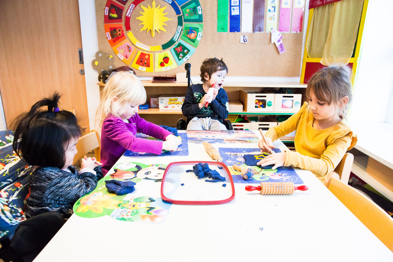 Kinder mit und ohne Behinderungen, die an einem Tisch sitzen und basteln und spielen