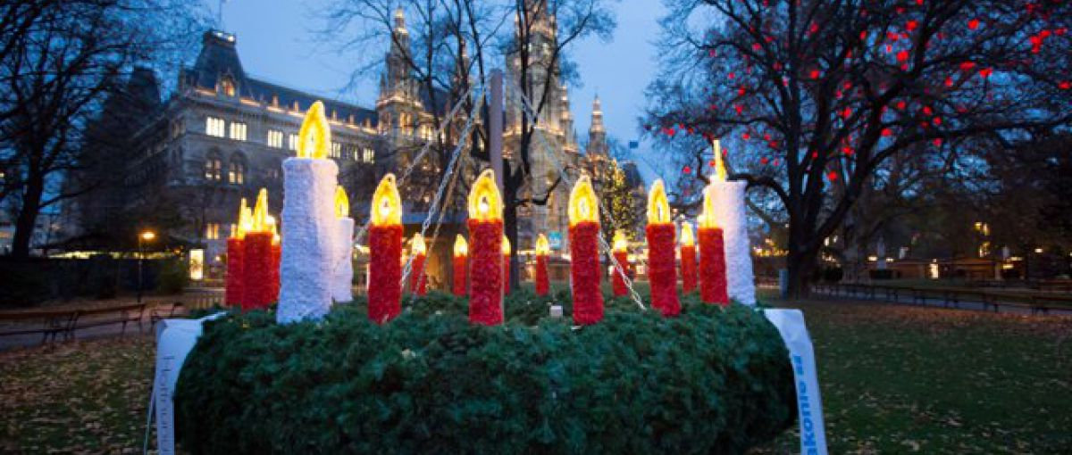 Ein großer Wichern-Adventkranz mit leuchtenden Kerzen steht im Rathauspark vor dem Wiener Rathaus.