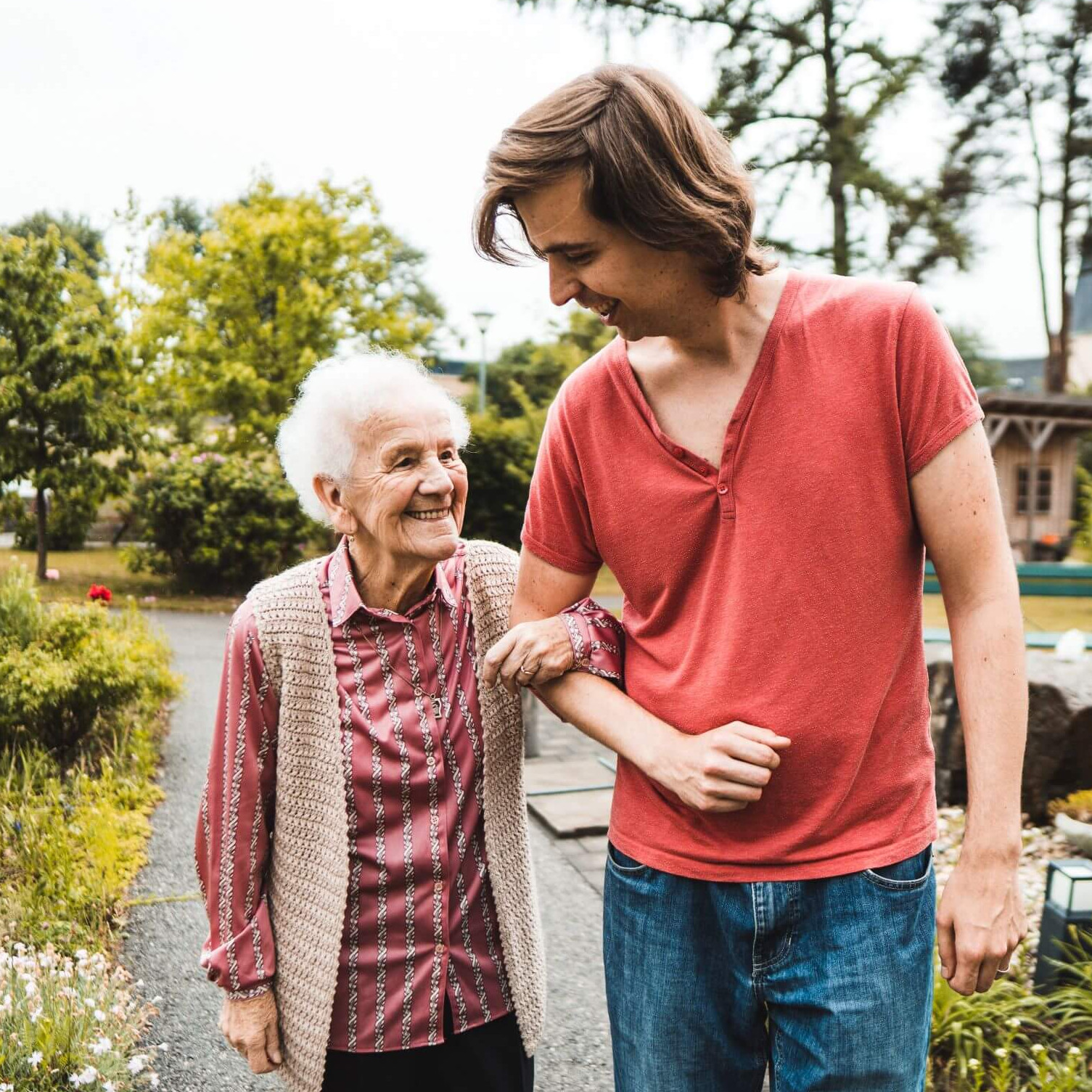 Ein junger Mann und eine lachende ältere Dame spazieren Arm in Arm.