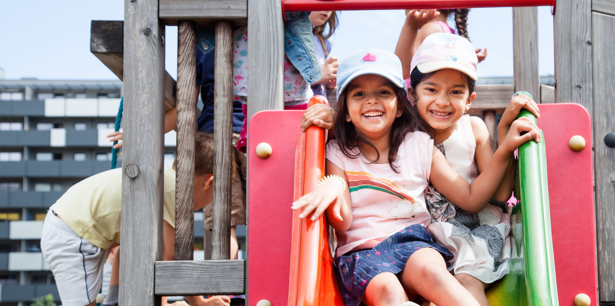 Zwei kleine Mädchen sitzen lachend auf einer Rutsche im Kindergarten Citygate der Diakonie Bildung