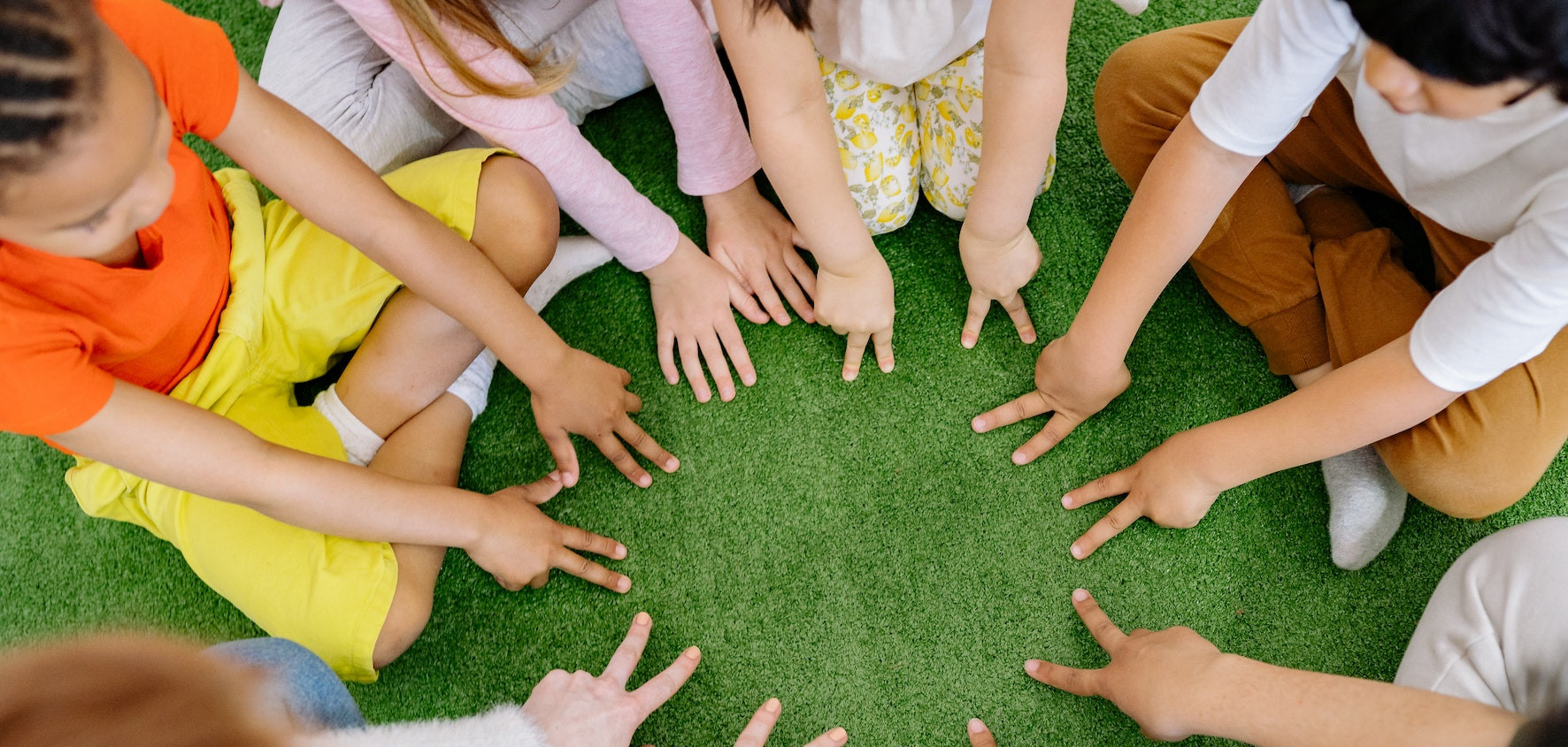 Kinder sitzen am Boden im Kreis und bilden mit den Fingern einen Kreis