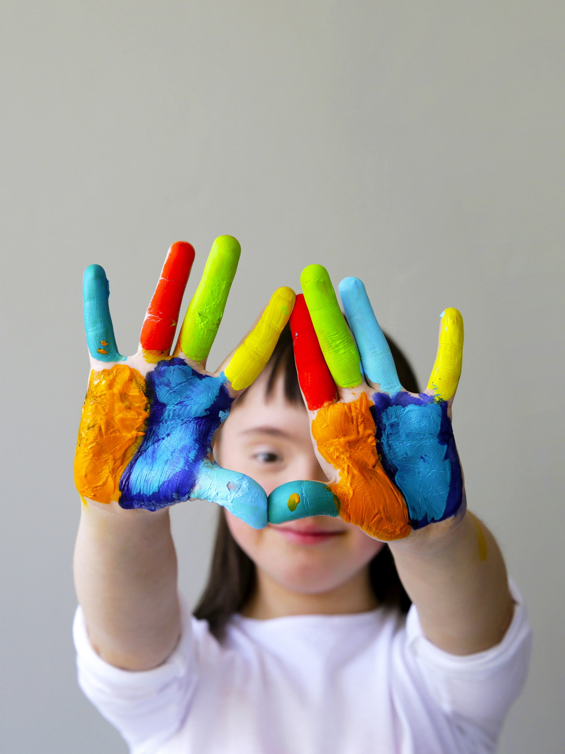 Ein Mädchen hält ihre zehn bunt bemalten Finger in die Kamera.