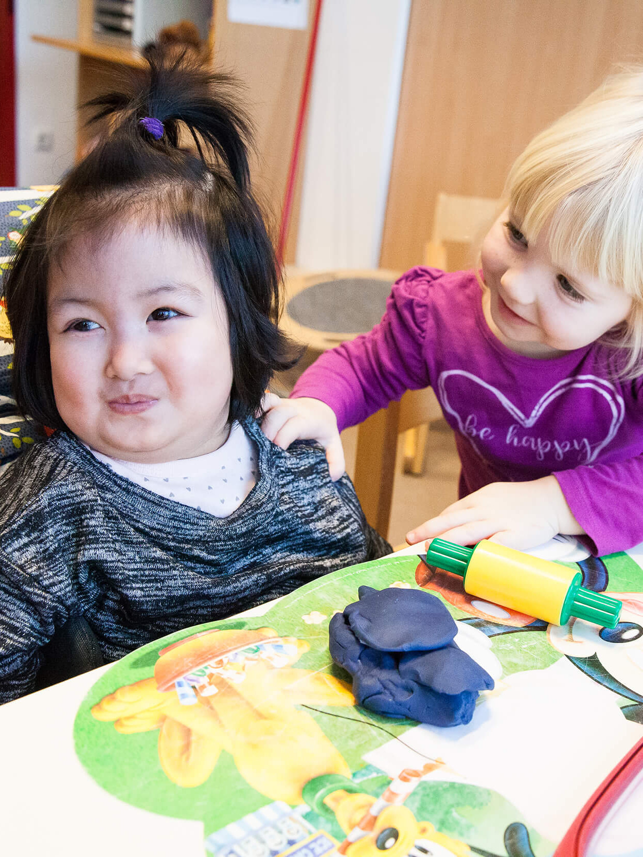 Zwei Kinder beim Spielen mit Knetmasse. Eines der Kinder sitzt im Rollstuhl.