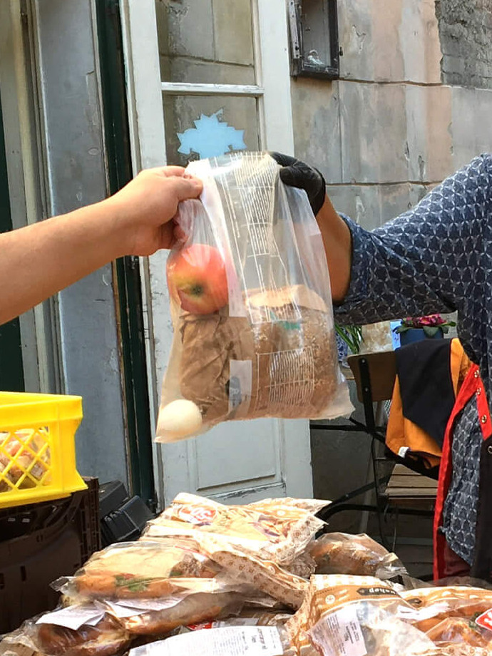 Eine Diakonie-Mitarbeiterin überreicht einem Gast ein Sackerl mit Essen zum Mitnehmen.