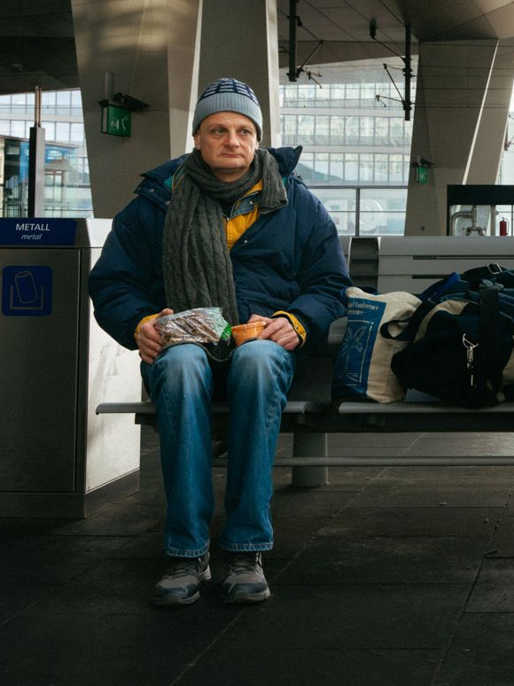 Mann sitzt auf Bank am Bahnsteig eines Bahnhofs