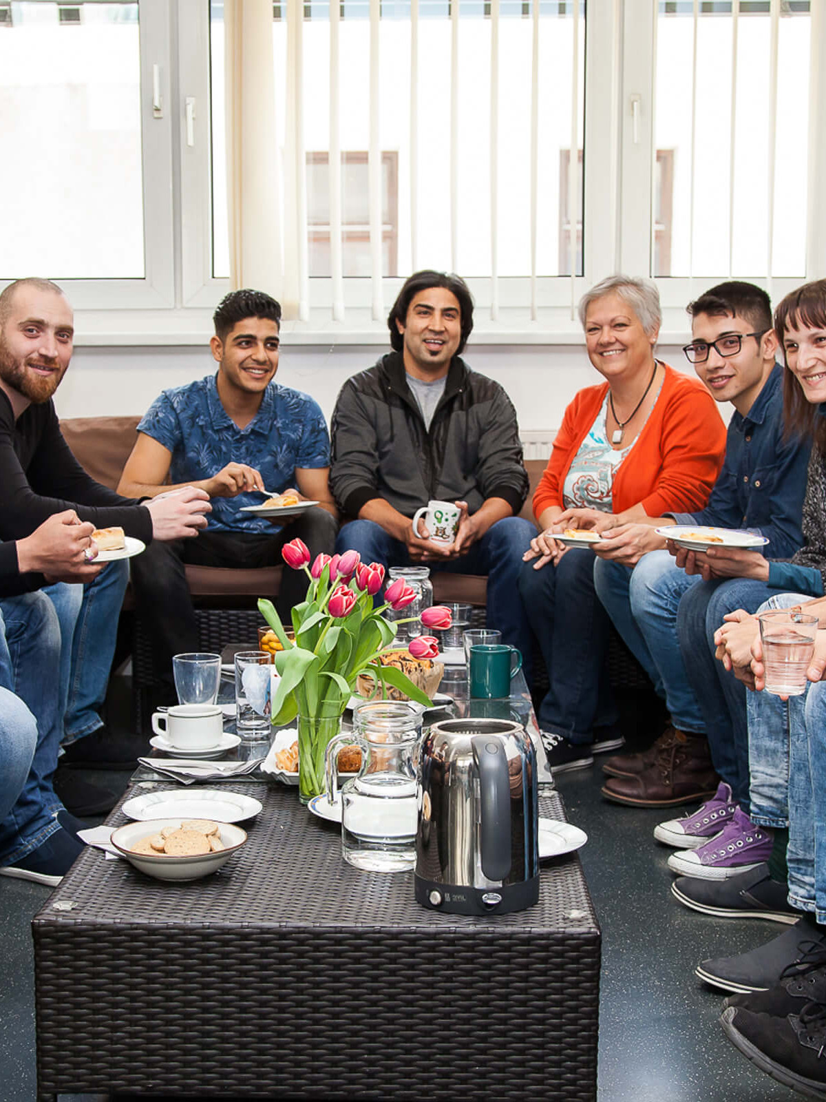 Eine gruppe von Menschen sitzt bei Kaffee und Kuchen um einen Tisch.