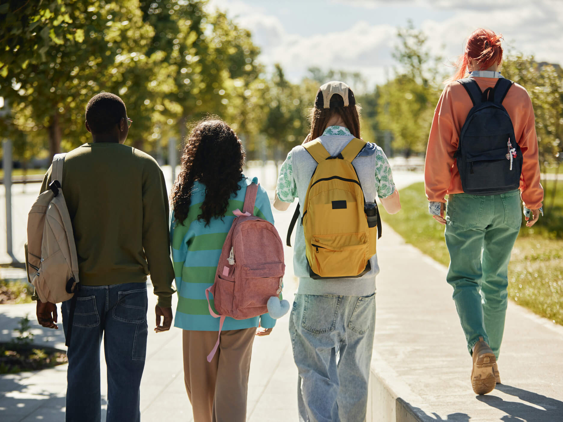 Vier junge Erwachsene gehen einen sonnigen Weg entlang durch einen Park