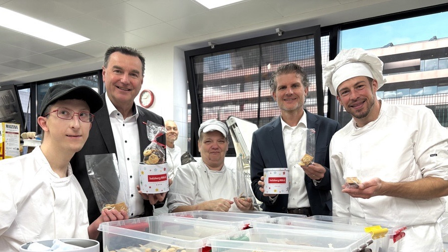Andreas Gasteiger und Florian Schwap (SalzburgMilch) stehen mit einem Fachmitarbeiter und KlientInnen des Kulinarium in einer Küche zusammen und halten Kekse und eine Keksdose in die Kamera.