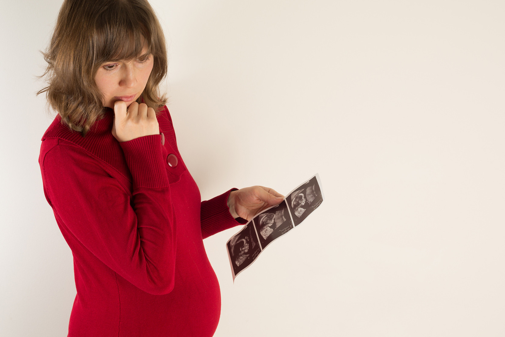 Schwangere Frau mit sorgenvollem Blick und Ultraschallbildern ihres Babys.