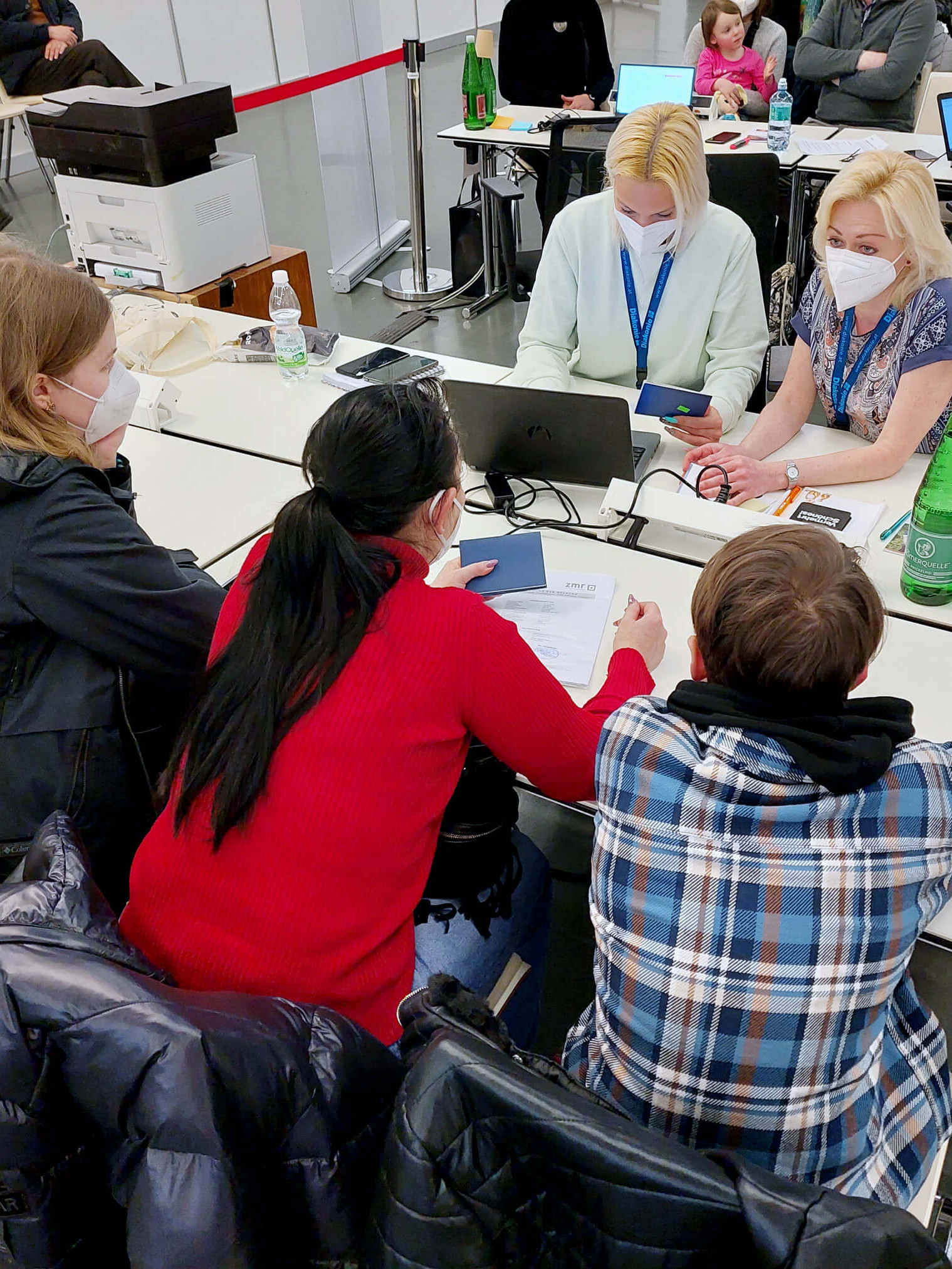 Beratungssituation im Austria Center Vienna: Zwei Frauen und ein Bub werden von zwei Mitarbeiterinnen der Diakonie beraten.